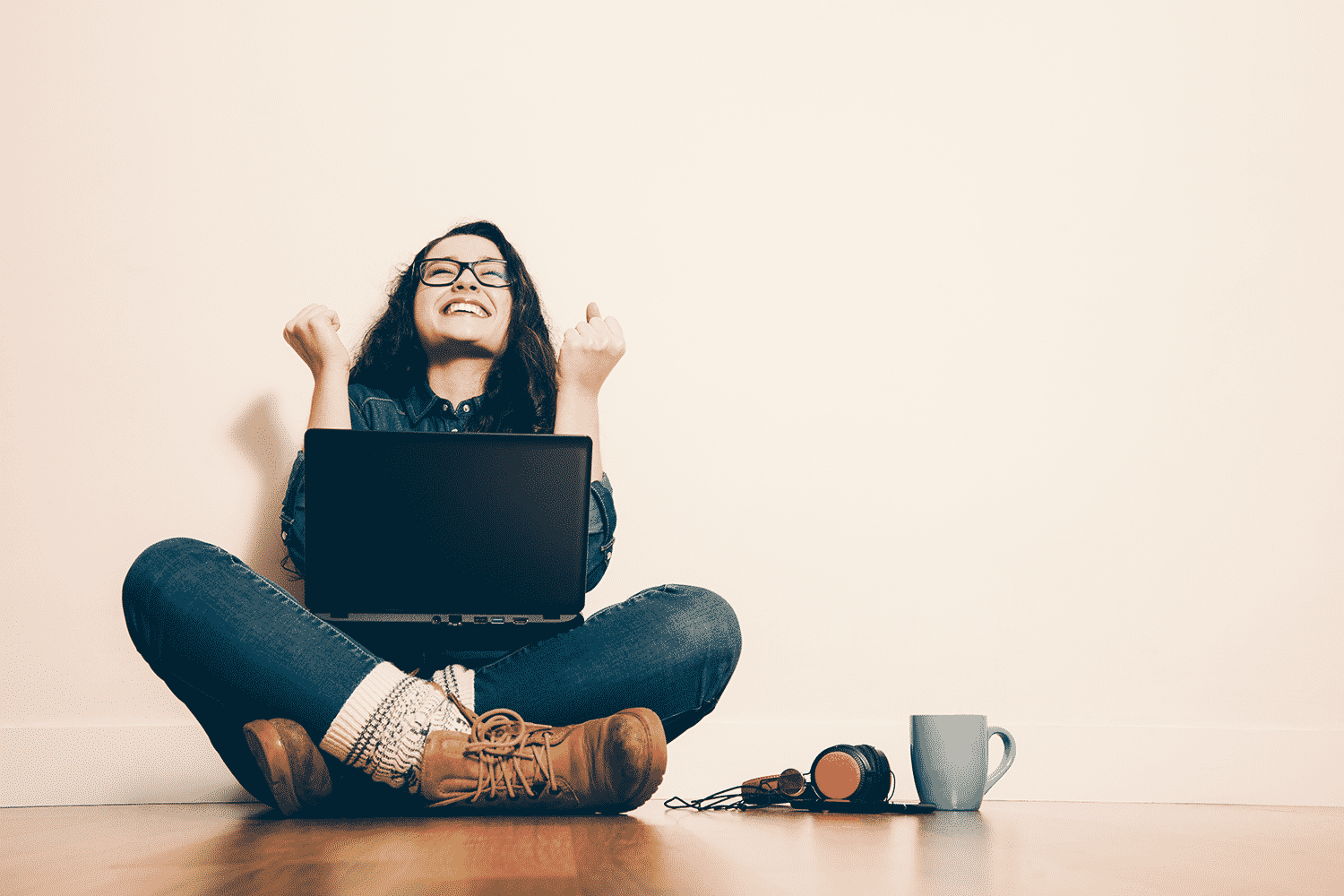 Young woman with laptop smiling with headphones and coffee next to her.